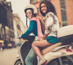 To piger på en cremefarvet scooter